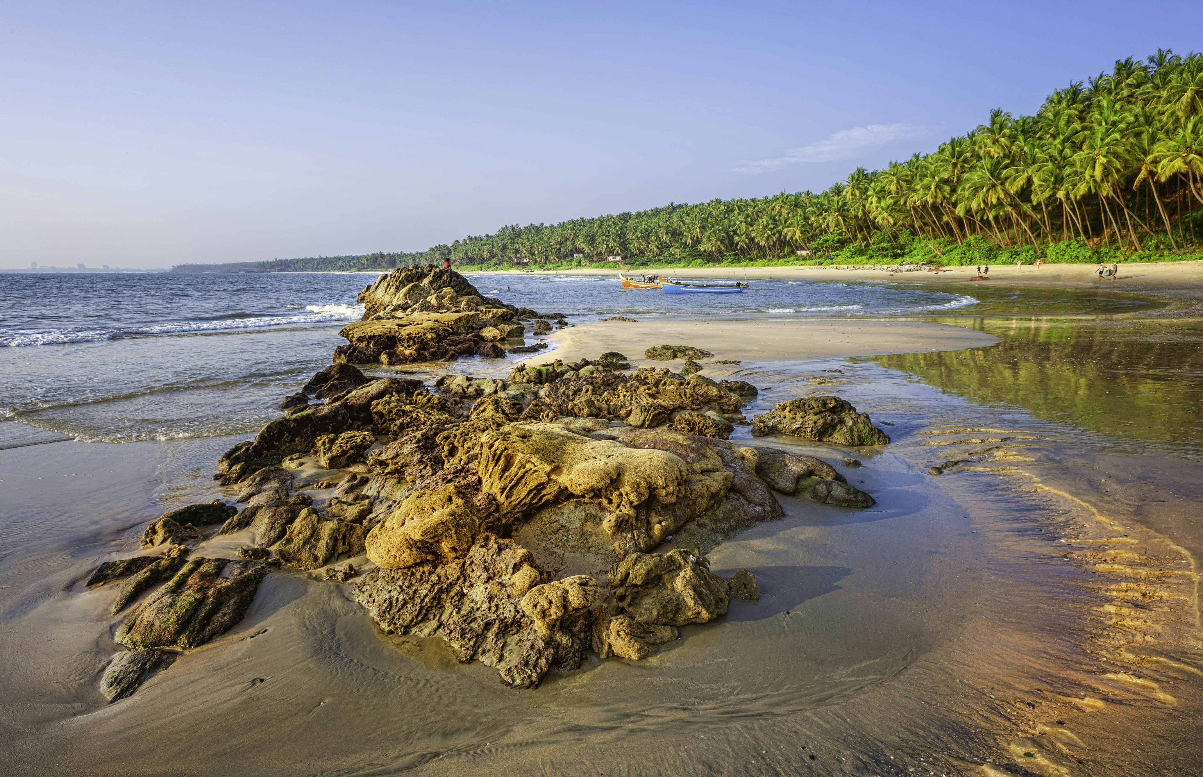 Kannur, December 10, 2011: Sunbathers and fishermen with boats on Cherai beach showing rocks formations in the foreground and coconut palms as backdrop at sunset along Malabar coastline, Kannur, Kerala, south India.